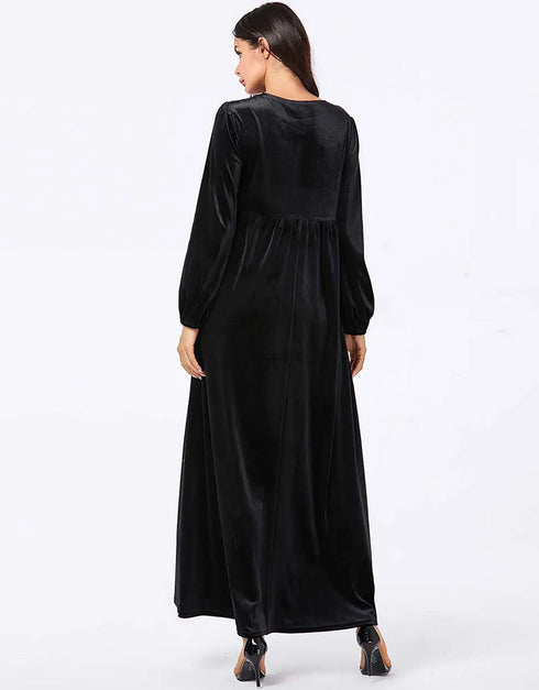 A flowing black or emerald green velvet abaya with delicate gold embroidery around the cuffs and neckline